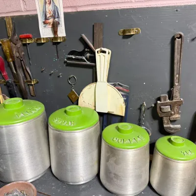 Vintage mid-century spun aluminum kitchen canister set with green plastic lids, labeled for flour, sugar, coffee, and tea.