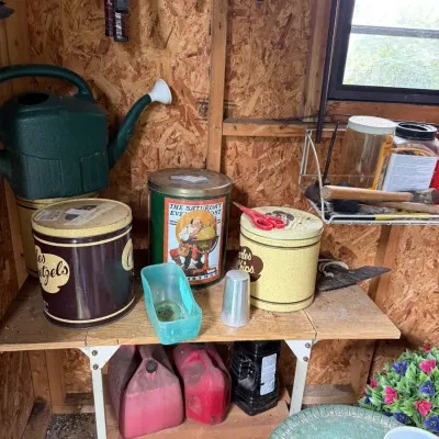 Assorted vintage tins, including Charles Chips and Charles Pretzels, displayed alongside a green watering can and various workshop items...
