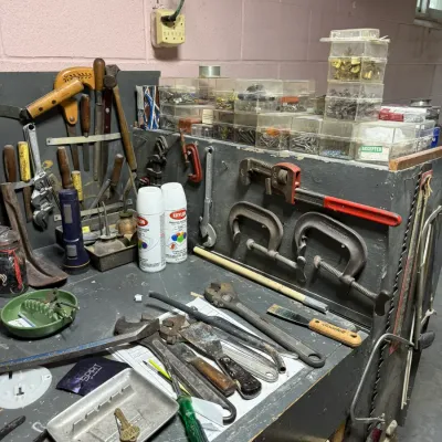 Assorted vintage hand tools, including wrenches, C-clamps, and screwdrivers, arranged on a grey wooden workbench with stacked plastic...