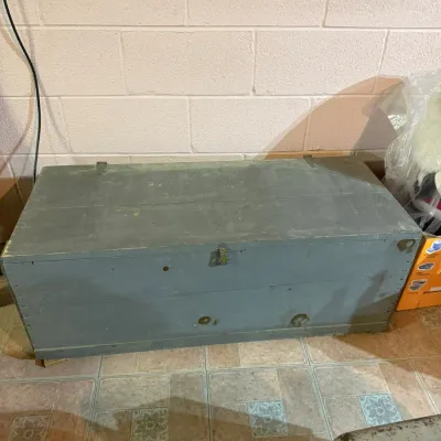 Vintage wooden storage chest painted in a muted blue-gray finish, featuring a hinged lid and simple metal latch.