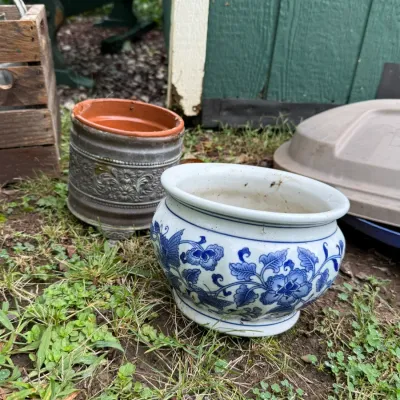 Vintage blue and white ceramic planter with floral and butterfly motifs, shown alongside a textured grey metal planter sleeve.
