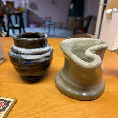 Two small, hand-thrown studio art pottery vessels, including a dark blue and white ribbed vase and a light green organic-shaped cup.