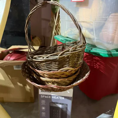 Stack of woven wicker baskets, including one with a high handle, resting on top of a boxed Riomor space heater.