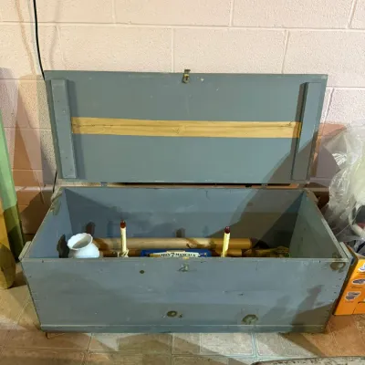 Vintage painted wooden storage chest in slate blue, shown open with various household items stored inside.