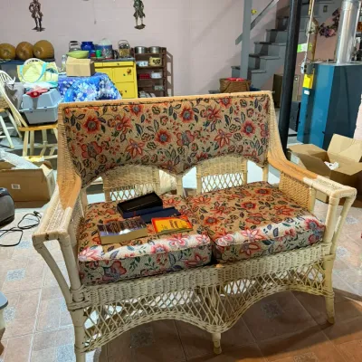 Vintage white wicker settee featuring floral patterned cushions in shades of red, blue, and green.