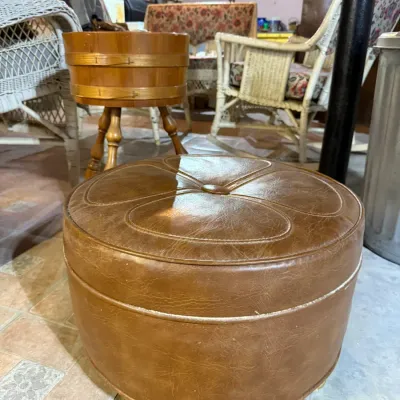 Vintage round brown vinyl ottoman with a tufted button top and decorative stitching, shown alongside other basement furniture.