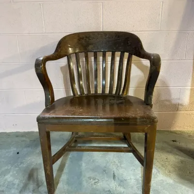 Vintage oak banker's chair with a curved slat back and contoured armrests, showing significant wear and patina to the dark finish.