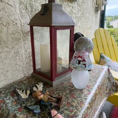 Assorted outdoor and holiday decor, featuring a large red and grey metal candle lantern, a small snowman-themed lamp, a mosaic sphere,...
