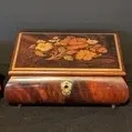 Three vintage Italian inlaid wood music boxes, featuring floral marquetry designs on the lids and small brass feet.