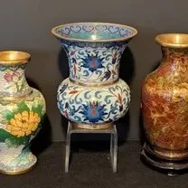 Three vintage Chinese cloisonné enamel vases in various shapes and floral patterns, including one on a wooden stand and one on an acrylic...