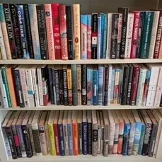 A white three-shelf bookcase filled with a large collection of assorted paperback and hardcover books.