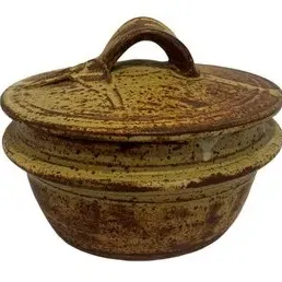Studio art pottery lidded casserole dish with a speckled brown and tan glaze and a prominent handle on the lid.