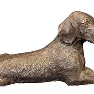Vintage cast metal dachshund figurine in a lying position, featuring a textured fur finish and a warm bronze-tone patina.