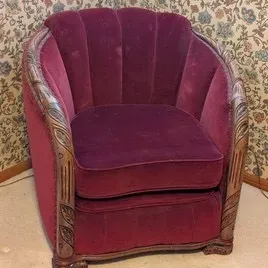 Vintage Art Deco style channel-back armchair upholstered in burgundy velvet, featuring carved wooden trim with leaf motifs along the arms.