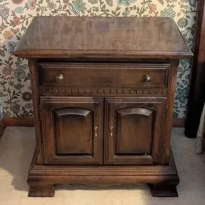 Traditional dark wood nightstand or accent cabinet featuring a single top drawer with brass pulls, two lower cabinet doors, and bracket...