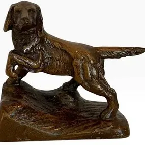 Vintage cast metal pointer dog figurine with a bronze-tone finish, depicted in a classic pointing stance on a textured base.