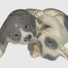 Royal Copenhagen porcelain figurine depicting two playful puppies, featuring a glossy glaze finish in shades of grey and white. Royal...