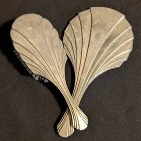 Vintage Art Deco silver-plated vanity set featuring a hairbrush and hand mirror with a matching fan or seashell motif.