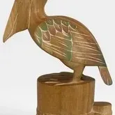 Hand-carved wooden pelican figurine perched on a piling, featuring painted wing details and an artist signature on the base.