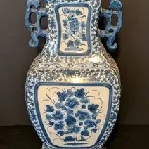 Vintage blue and white ceramic vase featuring hand-painted floral panels, ornate scroll handles, and a square base.