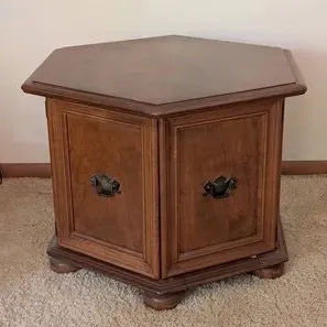 Vintage hexagonal wooden commode end table featuring double cabinet doors with metal pull handles and bun feet.