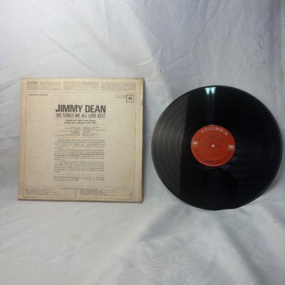 Sale Photo Thumbnail #22: Vintage vinyl record album featuring Jimmy Dean with "The Songs We All Love Best" on Columbia Records. Includes the original cardboard sleeve. The sleeve shows some age-related discoloration and wear along the edges, while the vinyl record itself appears 