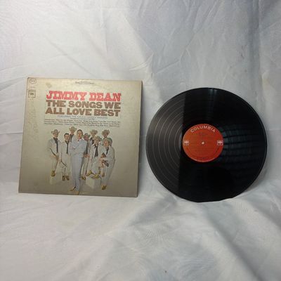 Sale Photo Thumbnail #21: Vintage vinyl record album featuring Jimmy Dean with "The Songs We All Love Best" on Columbia Records. Includes the original cardboard sleeve. The sleeve shows some age-related discoloration and wear along the edges, while the vinyl record itself appears 