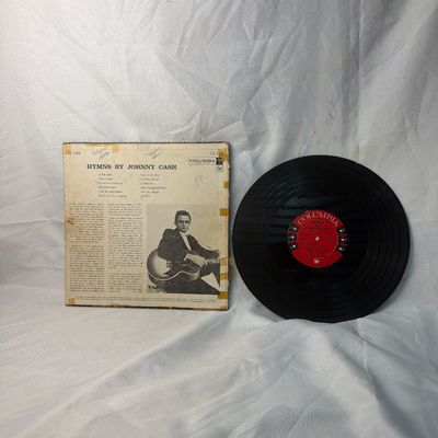 Sale Photo Thumbnail #43: Vintage vinyl record album 'Hymns by Johnny Cash' released on Columbia Records (CL 1284). Includes the original cardboard sleeve. The sleeve shows significant wear, including edge scuffing, discoloration, and tape residue. The vinyl record has a noticeabl