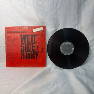 Sale Photo Thumbnail #27: Vintage vinyl record of the original soundtrack recording for "West Side Story" on Columbia Records (Stereo). Features the iconic red cover design. The cardboard sleeve shows some edge wear, corner scuffs, and a small price sticker on the front. The vinyl