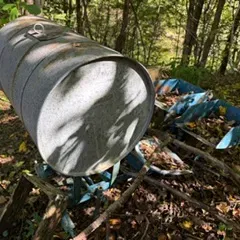 Vintage galvanized metal barrel train with blue painted cart bases, showing significant weathering and rust from outdoor storage.