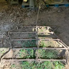 Vintage pull-behind spike tooth harrow, showing significant rust and wear from outdoor storage.