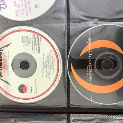 A collection of rock and metal CDs stored in a black binder, featuring Metallica's "...And Justice for All" and A Perfect...
