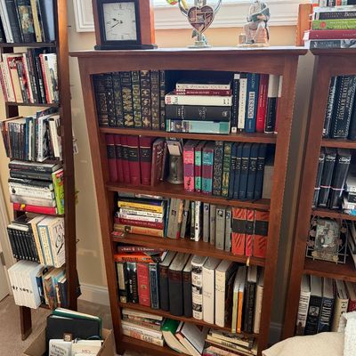 Tall cherry-finished wooden bookcase filled with a diverse collection of hardcover books, topped with a mantle clock and decorative...