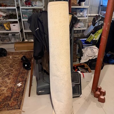 Large rolled area rug with a light-colored backing, standing upright in a basement storage area.