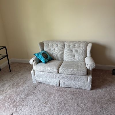 Traditional style loveseat with textured light gray upholstery, button-tufted back cushions, and a matching skirted base.