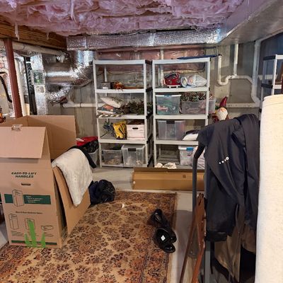 Unfinished basement storage area featuring plastic shelving units with holiday decor, a large patterned area rug, and cardboard moving...