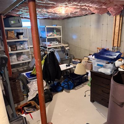 Assorted household goods, storage bins, shelving units, and fitness equipment in an unfinished basement storage area.