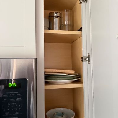 Assorted kitchenware including a floral ceramic baking dish, green-rimmed plates, and a stainless steel canister, displayed inside a...