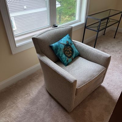 Contemporary upholstered swivel armchair in a neutral textured fabric, paired with a teal sea turtle accent pillow.