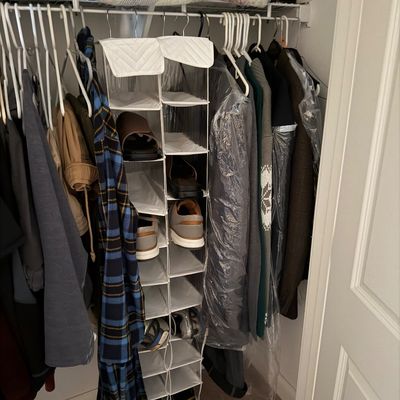 Assorted men's clothing, including jackets, sweaters, and a plaid robe, hanging in a closet alongside a hanging shoe organizer...