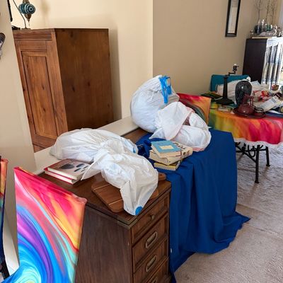 Vintage wooden desk with brass hardware, shown alongside chairs with vibrant rainbow-swirl slipcovers and various household items.