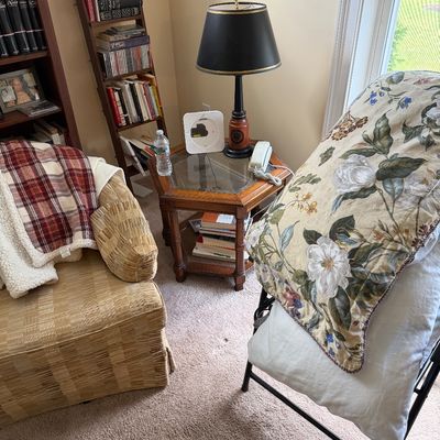 Cozy reading corner featuring a vintage hexagonal glass-top end table, a traditional table lamp with a black shade, and a comfortable...