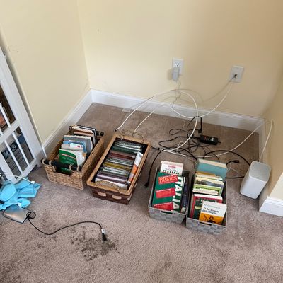 Assorted books and media organized in woven storage baskets on a carpeted floor.