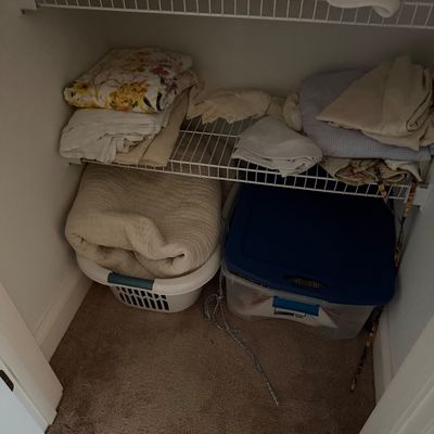 Assorted vintage bed linens, blankets, and towels organized on wire shelving and in storage bins inside a closet.