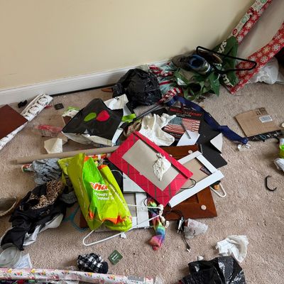 Assorted household clutter on a carpeted floor, including shopping bags, wrapping paper rolls, picture frames, and clothing hangers.