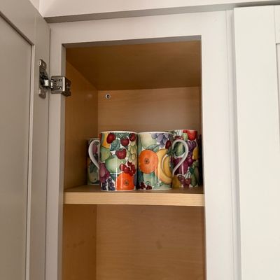 Set of ceramic mugs featuring a vibrant, all-over fruit motif, displayed inside a wooden cabinet.
