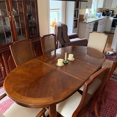 Traditional oval wooden dining table with an extension leaf, paired with cane-back chairs featuring upholstered seats.
