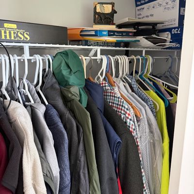 Assorted men's clothing including jackets, sweaters, and button-down shirts hanging in a closet, with board games and office...