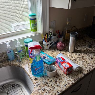 Assorted household cleaning supplies, hand soaps, and kitchen items arranged on a granite countertop next to a sink.
