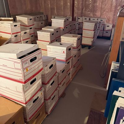 Large collection of numbered cardboard banker boxes stacked in a basement storage area, likely containing documents, records, or...